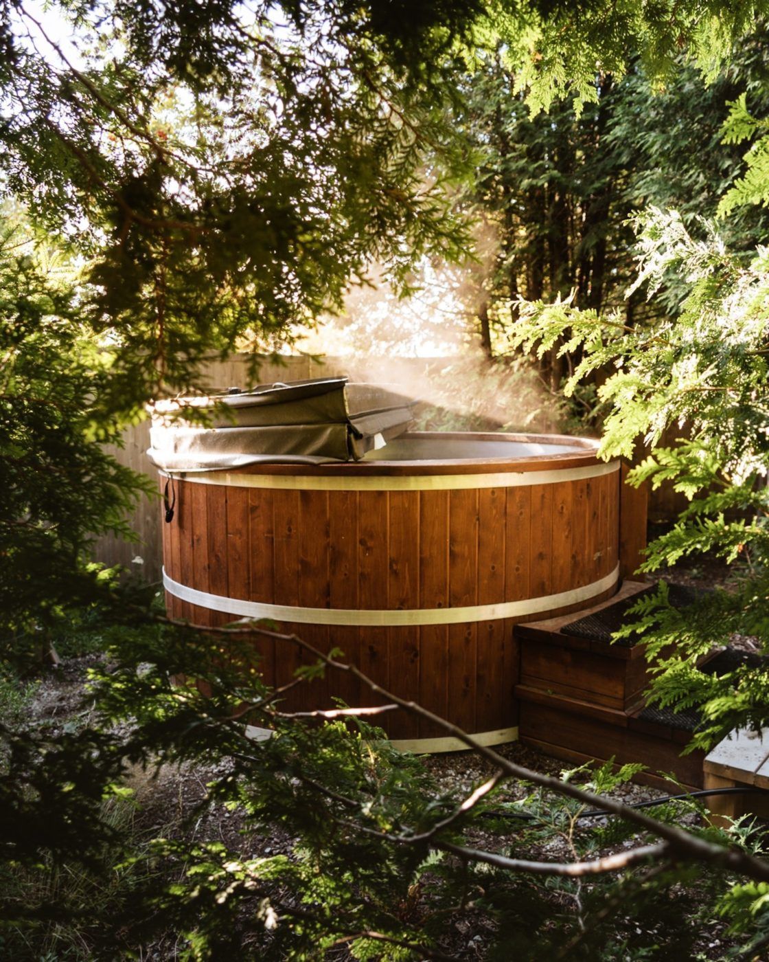 Een houten jacuzzi, omgeven door weelderig groen, waar het zonlicht door de bomen filtert.