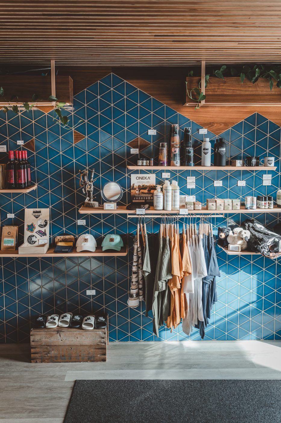 Een muur met blauwe tegels, planken, hangende kleding en serviesgoed in een gezellig winkelinterieur.