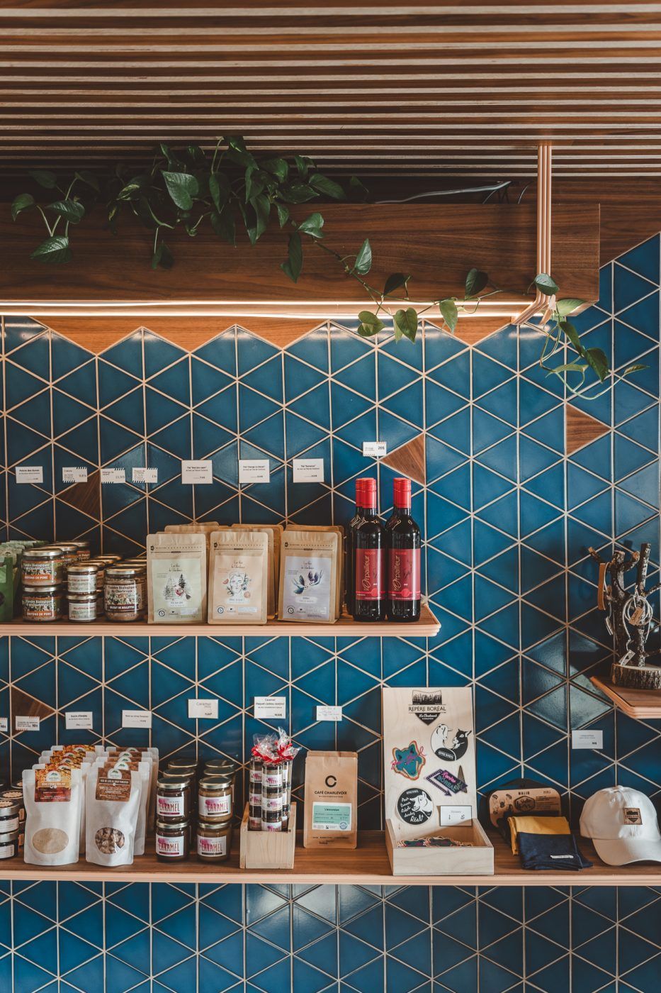 Een schap met koffiebonen en verpakte producten tegen een blauwe, geometrische tegelwand in een café of winkel.