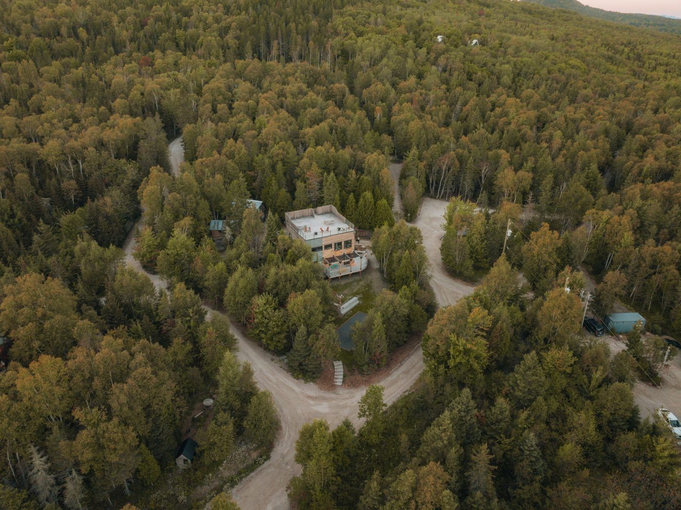 Luchtfoto van een huis verscholen in een dicht bos met kronkelende onverharde wegen.