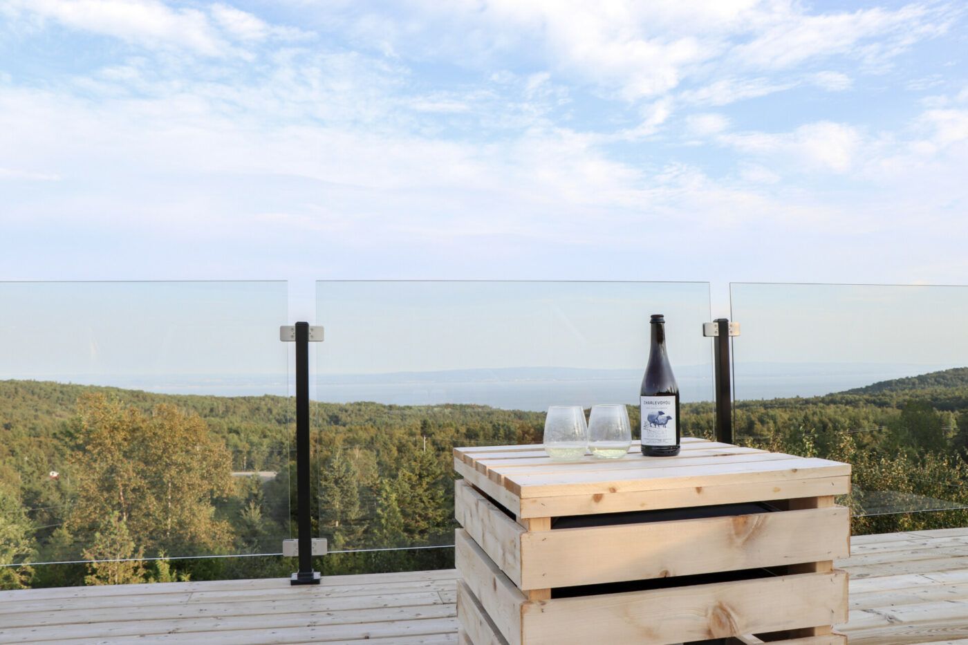 Wijnfles en glazen op een houten krat met uitzicht op een schilderachtig terras op een heuvel met glazen balustrade.