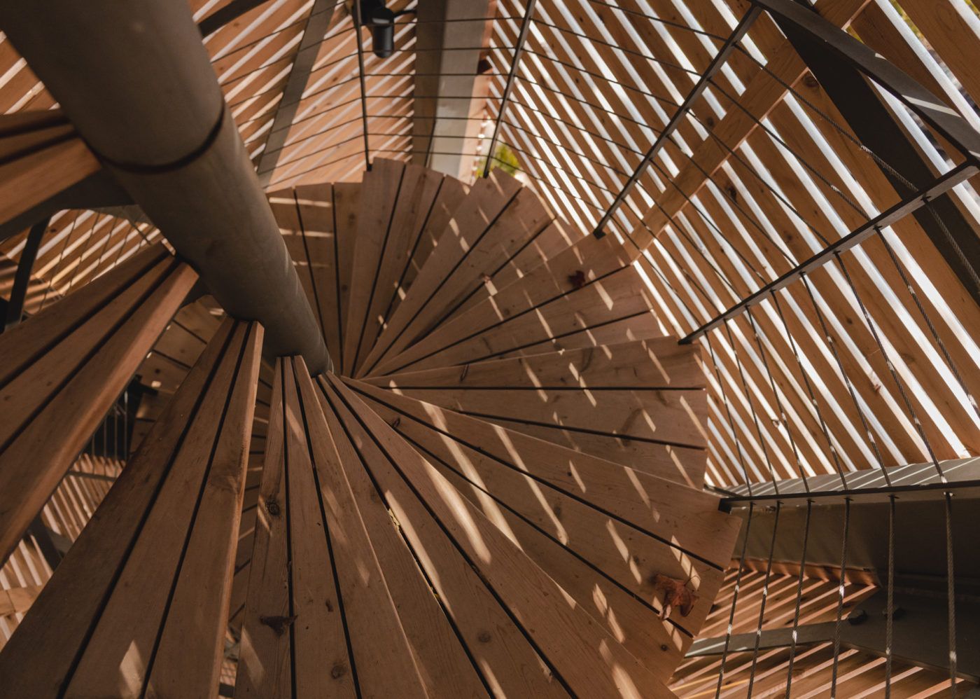 Close-up van een houten wenteltrap met schaduwen van latten en warm licht.