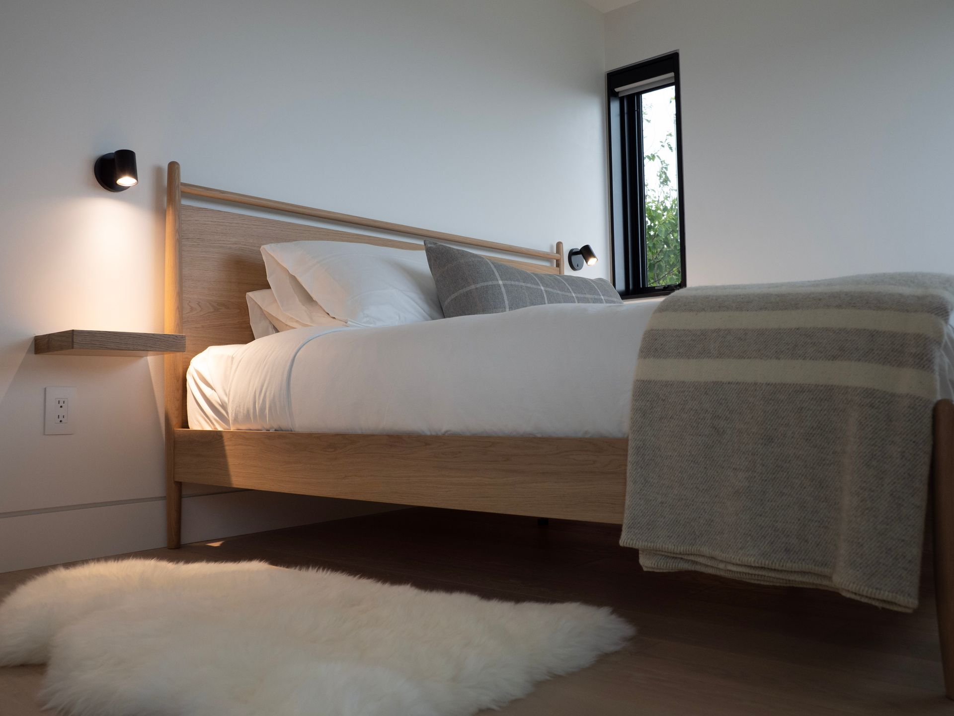 Minimalistische slaapkamer met een houten bed, wit beddengoed, wandlampen en een zacht vloerkleed.