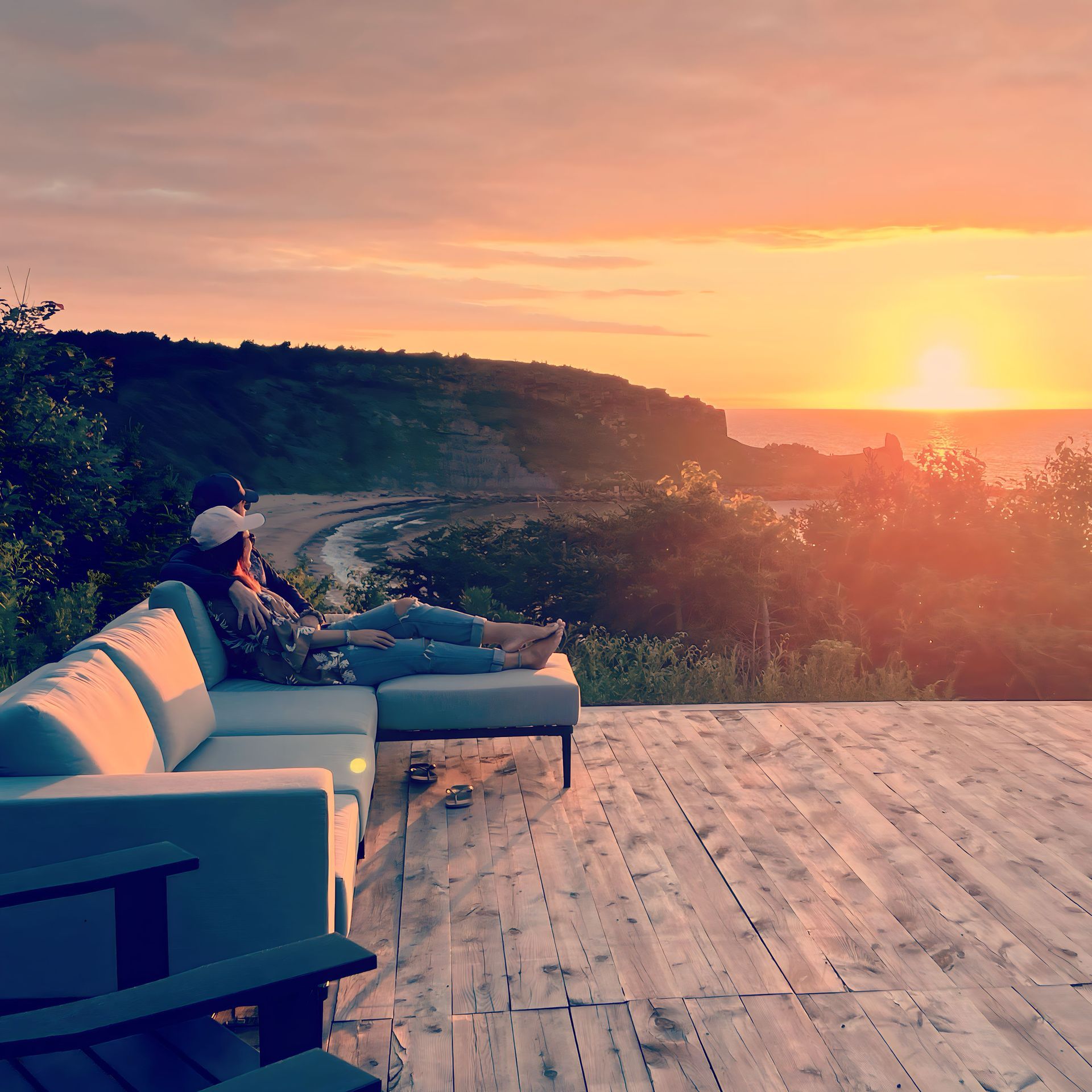 Een persoon ontspant op een terrasstoel bij zonsondergang, met uitzicht op een klif aan de kust en de glinsterende oceaan.