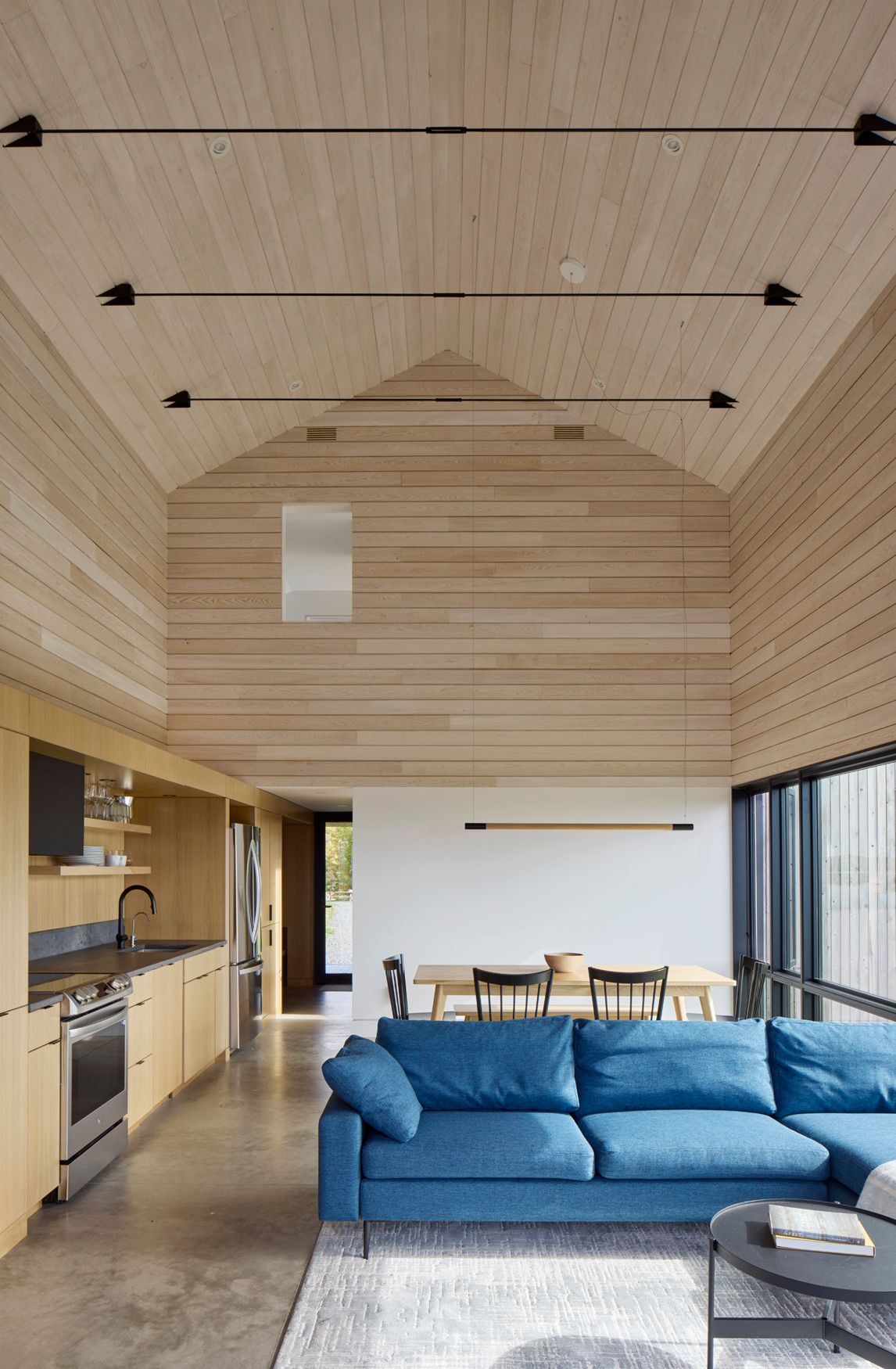 Moderne open woonkamer met blauwe hoekbank, houten plafond, keuken en eethoek.