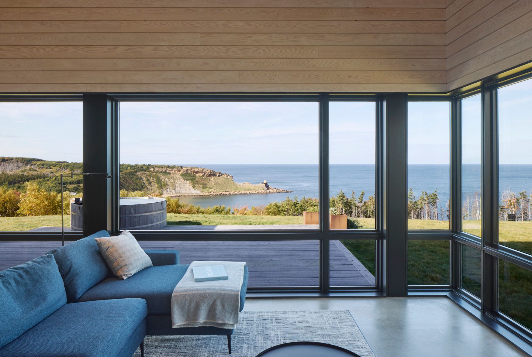 Moderne woonkamer met blauwe bank en uitzicht op de oceaan door grote glazen ramen.