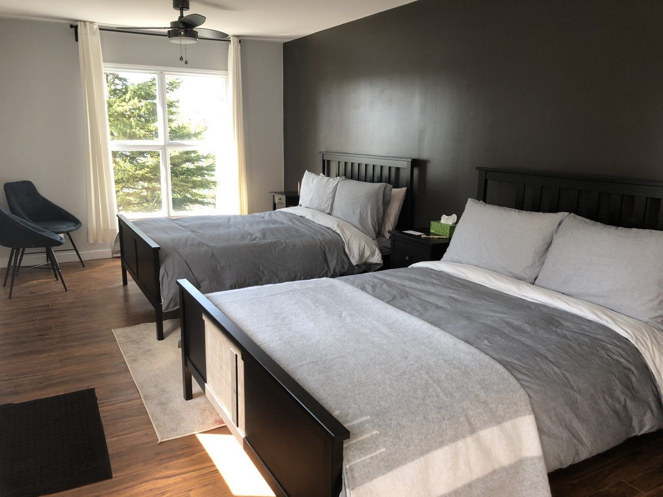 Ruime slaapkamer van Rock Island Lodge met twee grijze bedden, een raam, een donkere houten vloer en een plafondventilator.