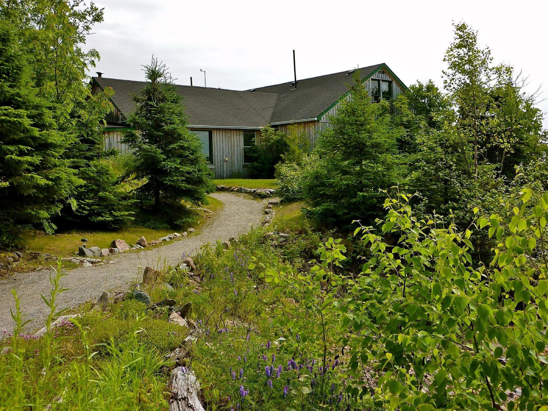 Een kronkelend grindpad door een weelderige groene tuin leidt naar een het hoofdgebouw van Rock Island Lodge met een verweerd dak.