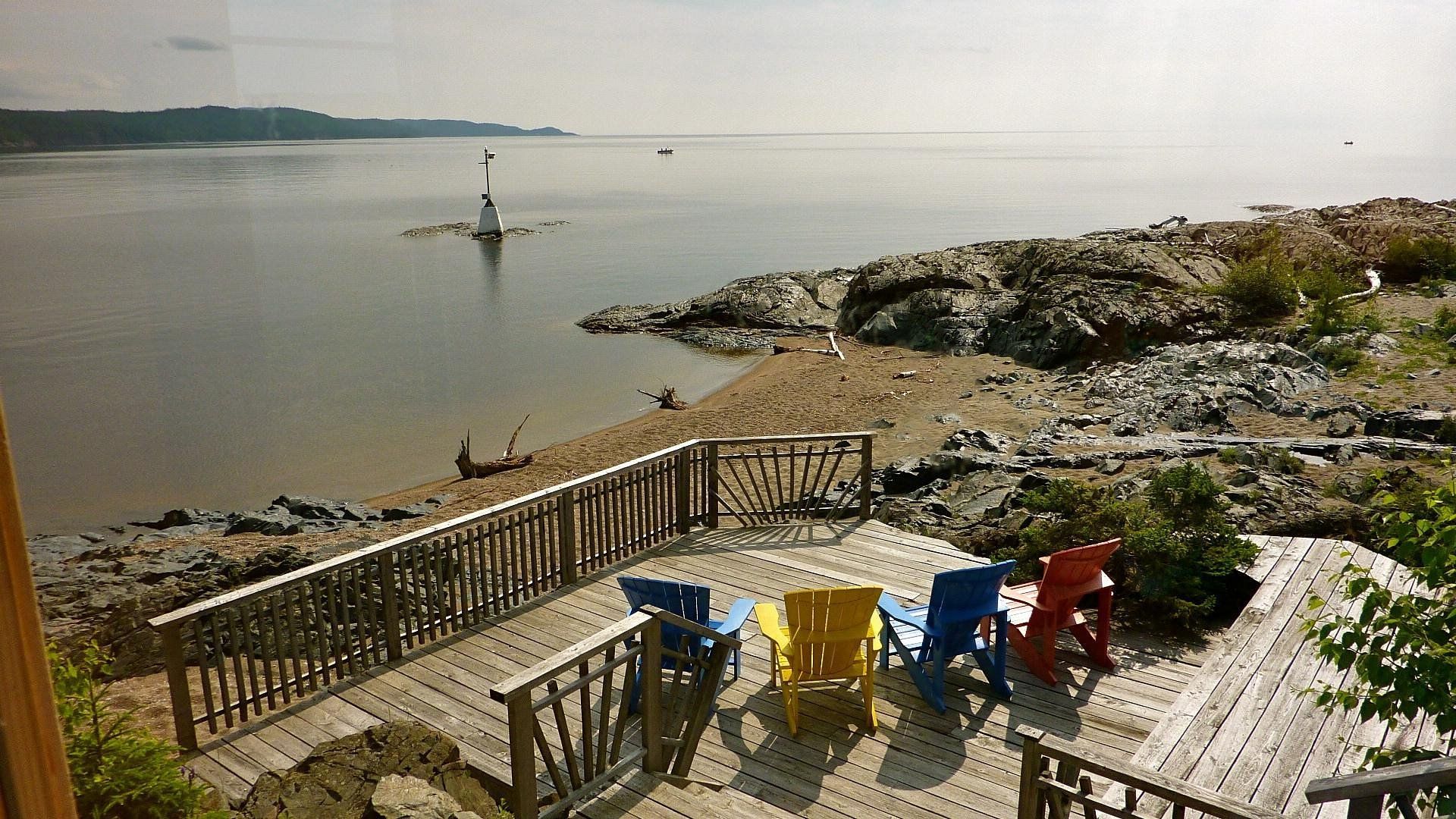 Kleurrijke stoelen op een terras van Rock Island Lodge aan zee met uitzicht op het kalme water en de rotsachtige kust bij zonsondergang.