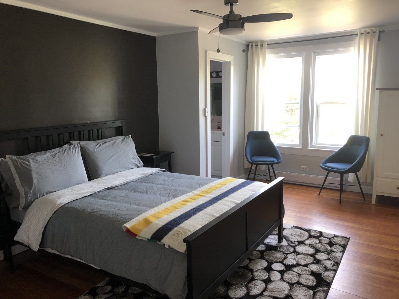 Moderne slaapkamer van Rock Island Lodge met zwart bed, grijs beddengoed, twee stoelen bij een licht raam en een vloerkleed met patroon.