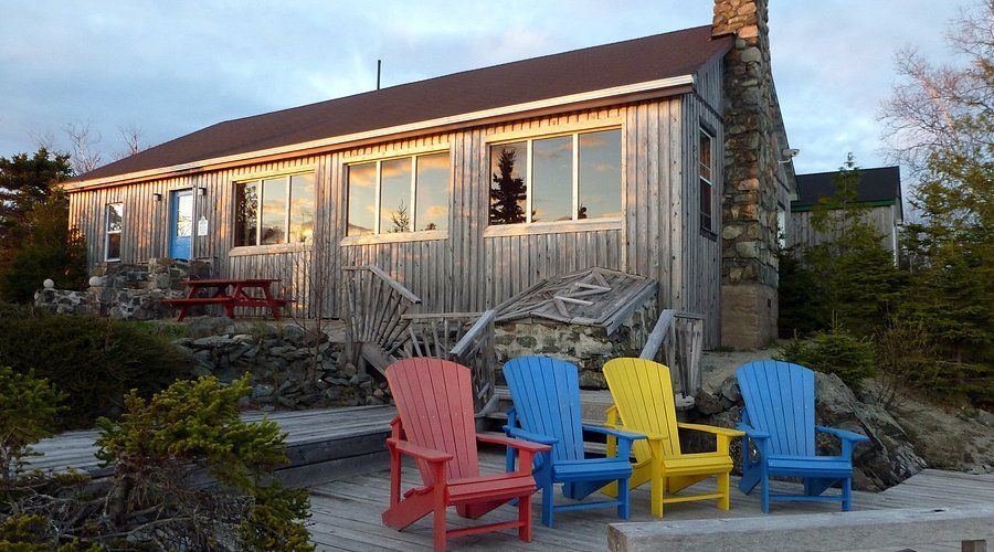 Kleurrijke Adirondack-stoelen op een terras buiten een rustiek stenen en het hoofdgebouw van Rock Island Lodge bij zonsondergang.