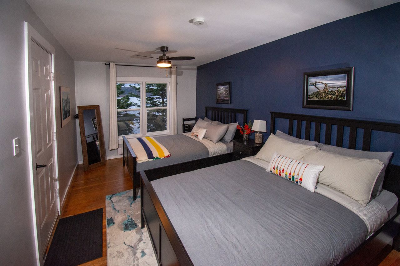 Moderne slaapkamer van Rock Island Lodge met twee bedden, een blauwe accentmuur en een groot raam aan het uiteinde.