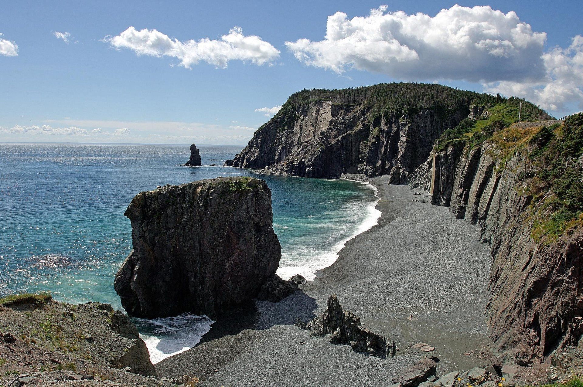 Rotsachtige kustklif en rotsformatie in zee op Newfoundland, Canada naast een blauwe oceaan onder een gedeeltelijk bewolkte hemel.