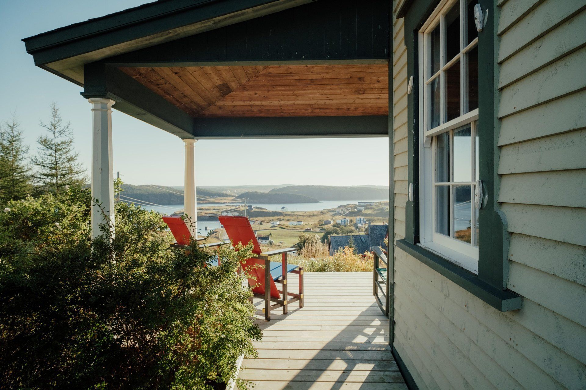 Veranda van Fisher's Loft Inn met twee rode stoelen met uitzicht op een zonnig kustplaatsje en de baai.