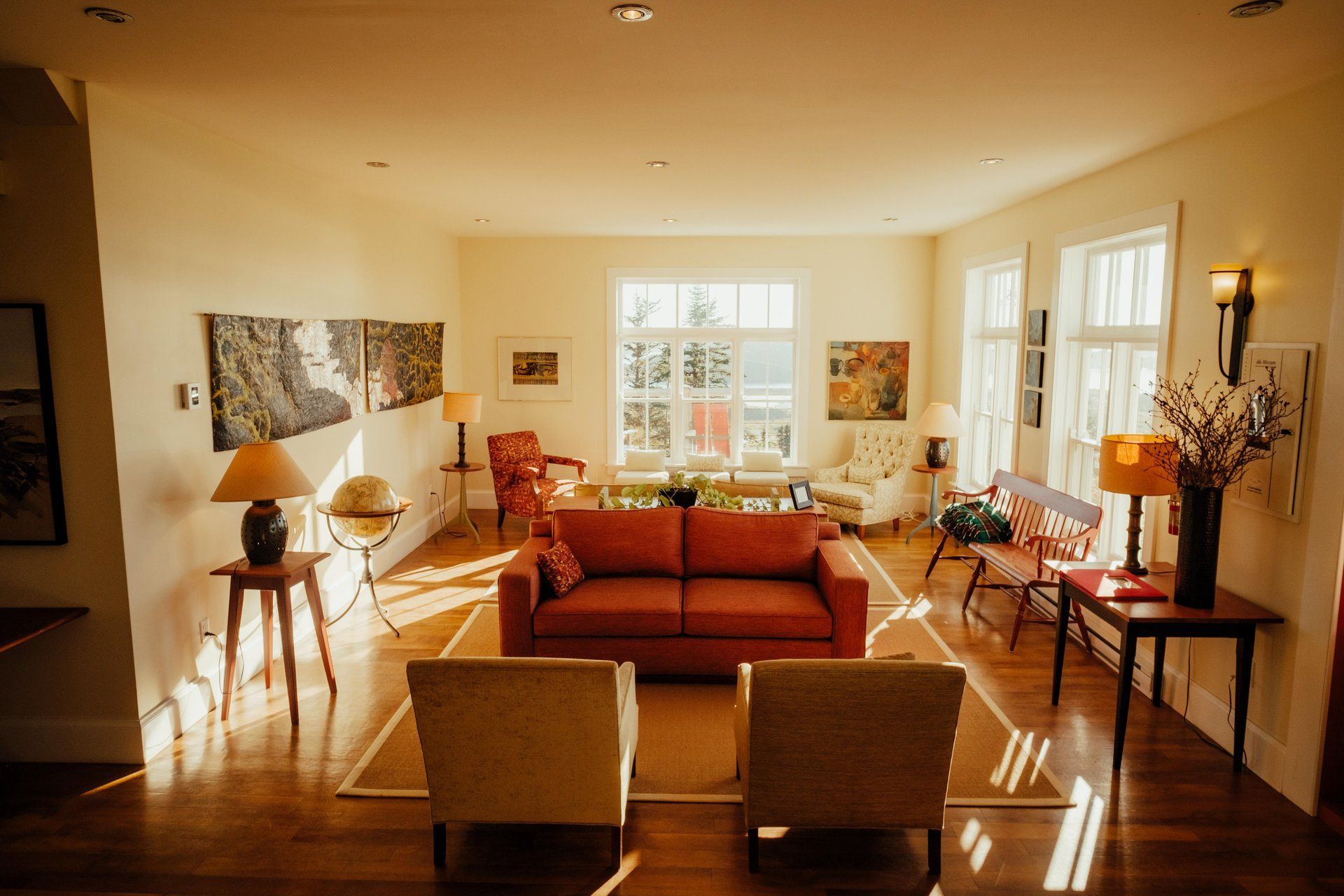 Lichte living van Fisher's Loft Inn in Port Rexton met oranje bank, twee fauteuils, houten tafel en ramen waar het zonlicht doorheen valt.