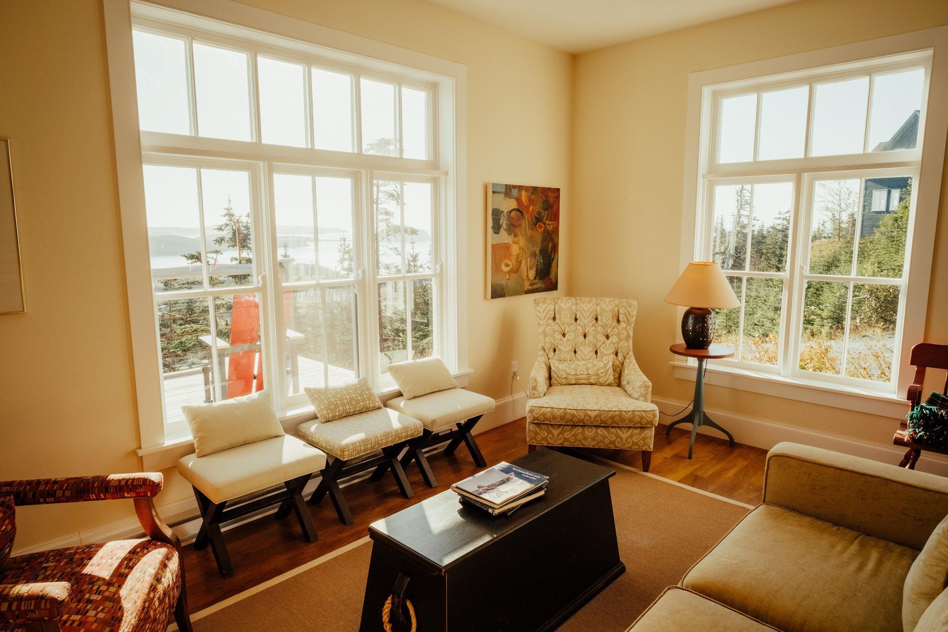 Gezellige woonkamer van Fisher's Loft Inn in Port Rexton met grote ramen, beige stoelen, bank, lamp en salontafel in het warme zonlicht.