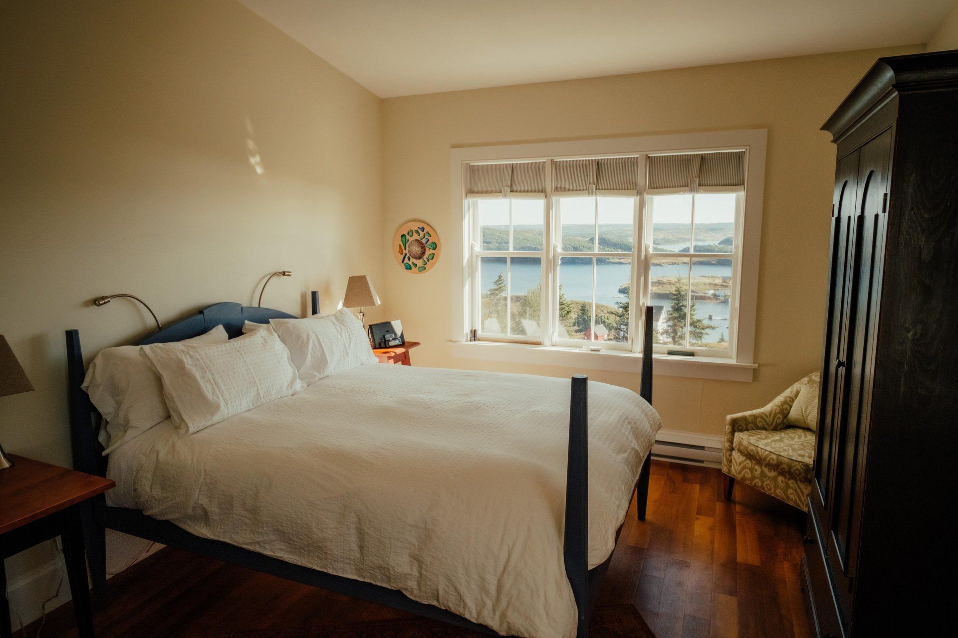 Lichte slaapkamer van Fisher's Loft Inn in Port Rexton met wit bed, houten vloer en groot raam met uitzicht op het water.