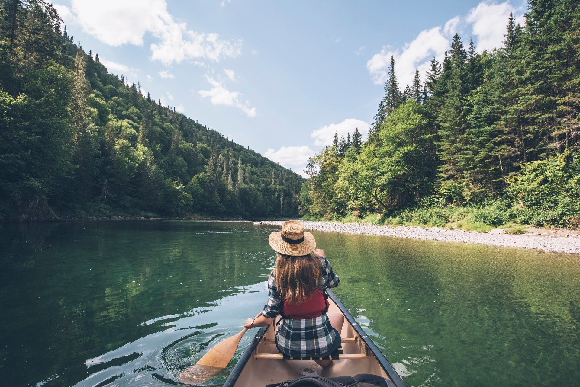 Een persoon in een kano op de Restigouche River in New Brunswick, Canada,, omringd door beboste bergen onder een heldere hemel.