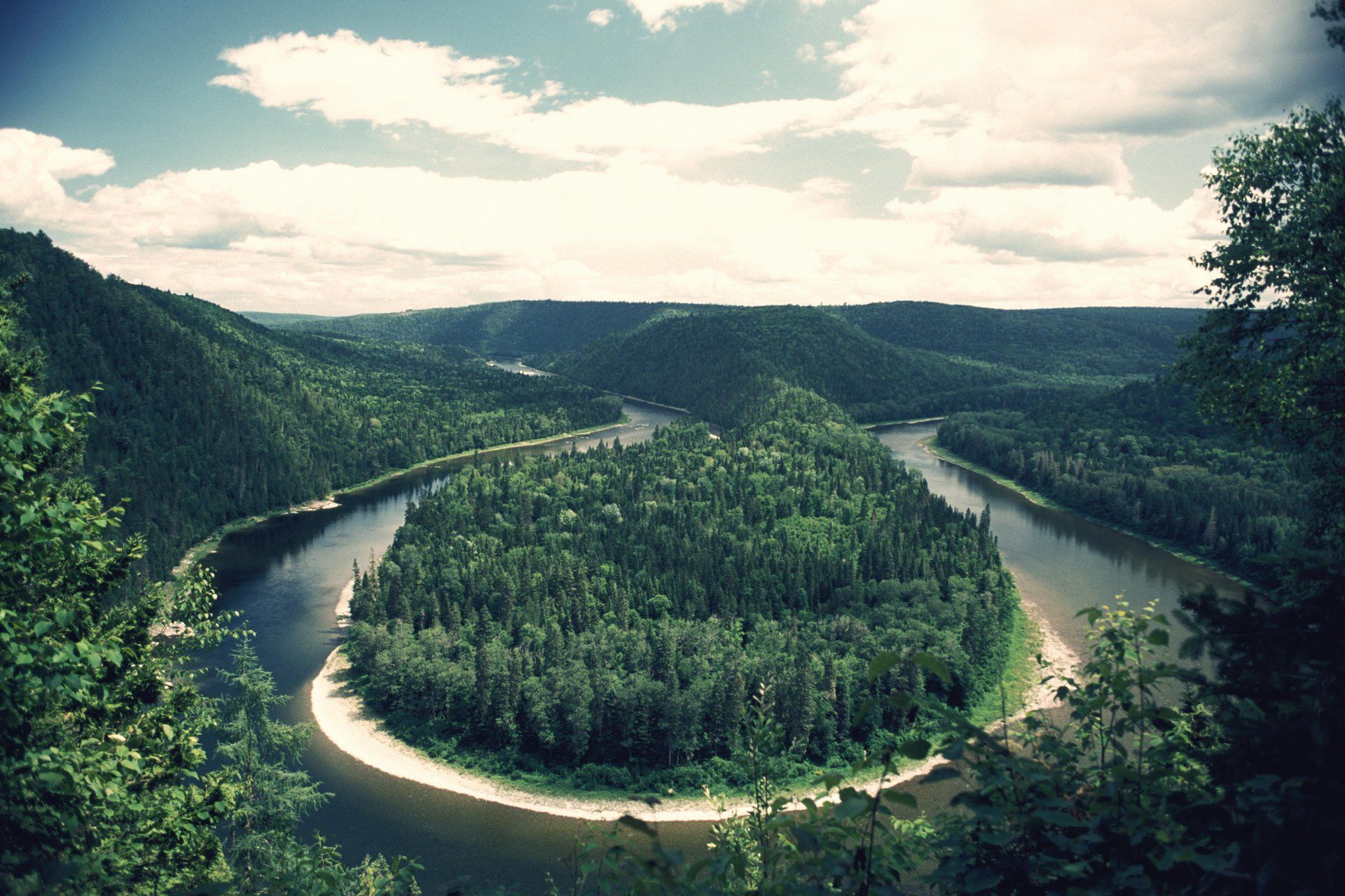 De Uitzicht op de Restigouche River in New Brunswick, Canada, kronkelt rond een bebost eiland in een groene vallei onder een bewolkte hemel.