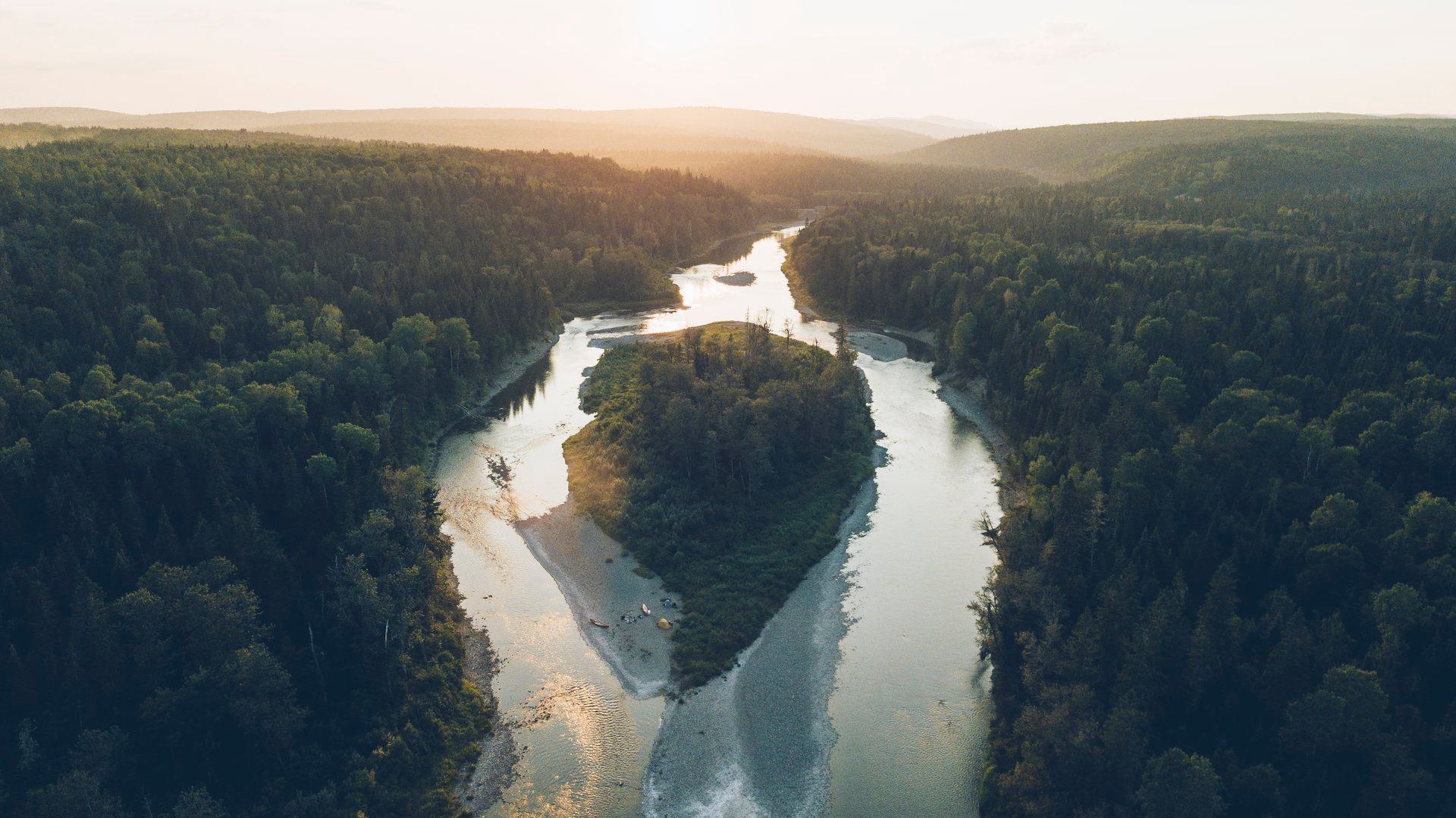 De Restigouche River in New Brunswick, Canada, die zich een weg baant door een dicht bos bij zonsondergang en een smal eilandje in het midden vormt.