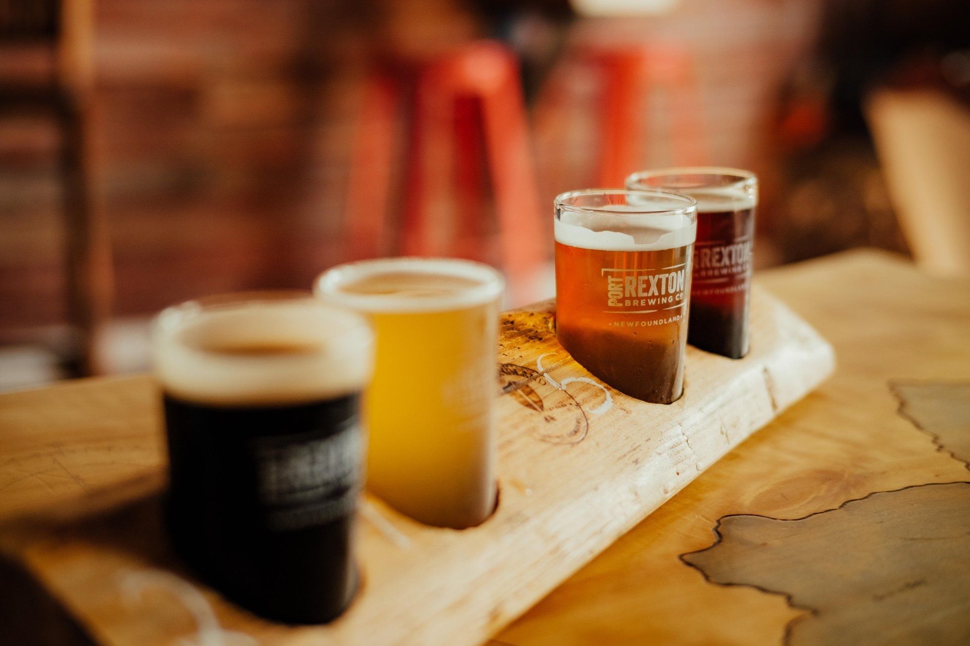Vier biertjes van Port Rexton Brewing in Canada op een houten dienblad op de bar, met een wazige, warmgetinte achtergrond.