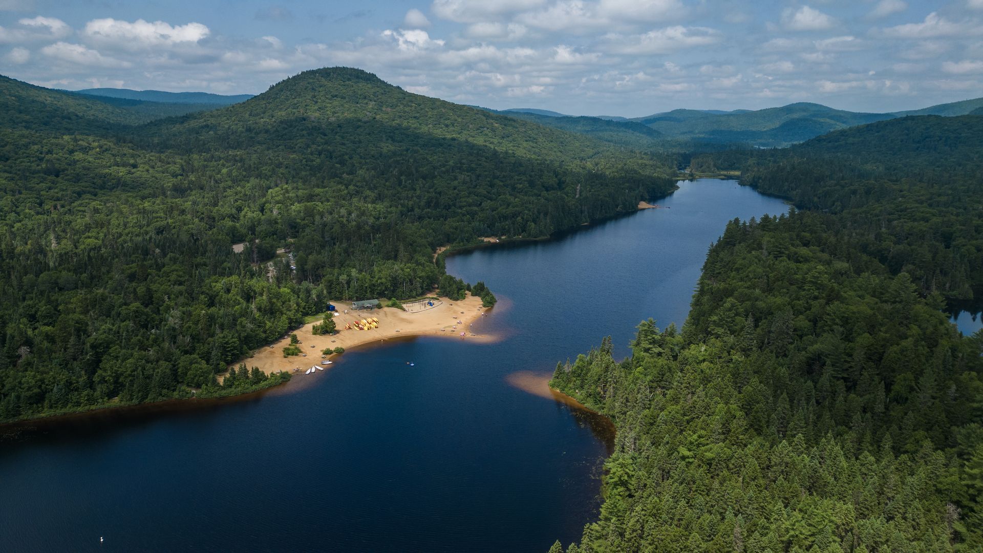 Luchtfoto van de kronkelende blauwe rivier en Lac Provost beach in het Parc national du Mont-Tremblant Lanaudière Canada in een dicht groen bos en heuvels onder een gedeeltelijk bewolkte hemel.