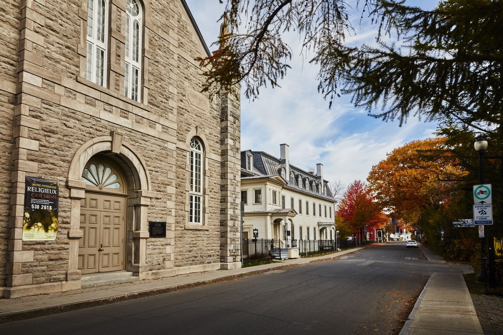 Stenen gebouw in een rustige straat in het plaatsje Trois-Rivieres te Quebec, Canada met herfstbomen en geparkeerde auto's onder een bewolkte hemel.