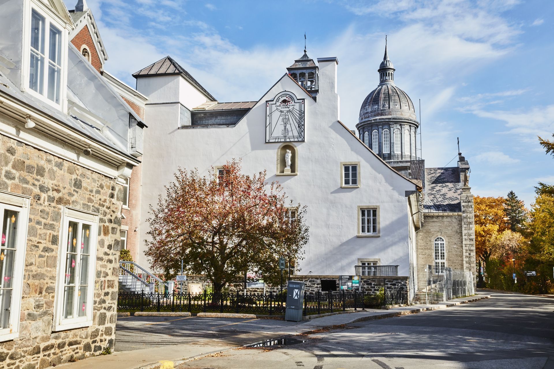 Historisch stenen gebouw in het plaatsje Trois-Rivieres te Quebec, Canada met witte puntgevel en herfstbomen onder een blauwe hemel.