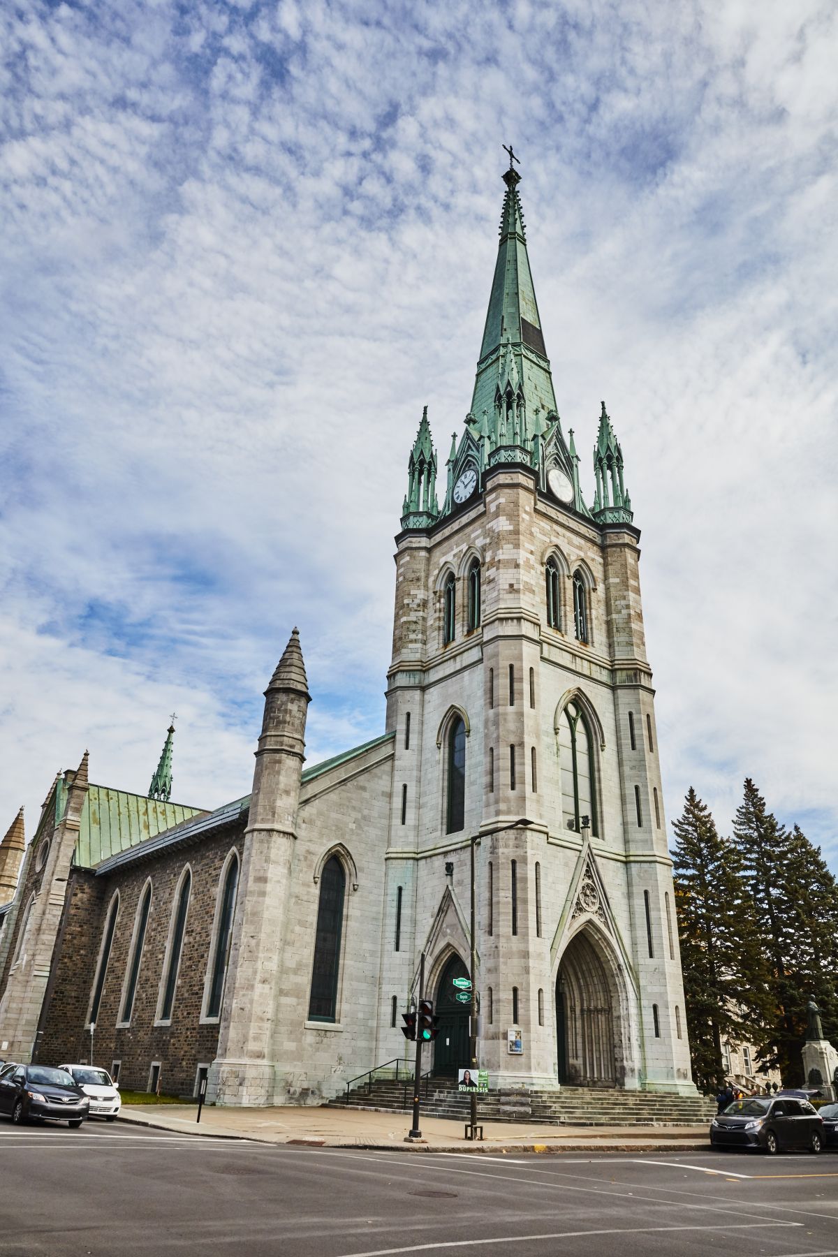 Gotische kerk in het plaatsje Trois-Rivieres te Quebec, Canada met een hoge groene torenspits en een stenen gevel, gelegen aan een straat onder een bewolkte hemel.
