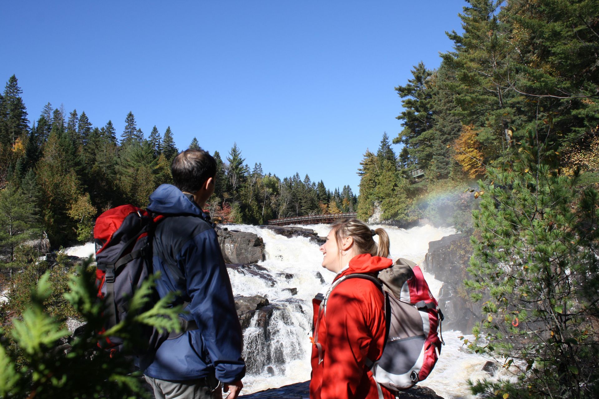 Twee wandelaars in Canada in rode jassen bekijken een waterval in een beboste kloof.