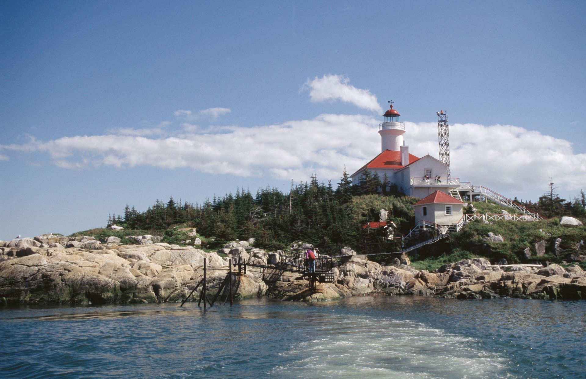 De rood-witte vuurtoren Brandy Pot Island Lighthouse in Quebec, Canada, op een rotsachtig eiland met bomen onder een blauwe hemel, gezien vanaf het water.