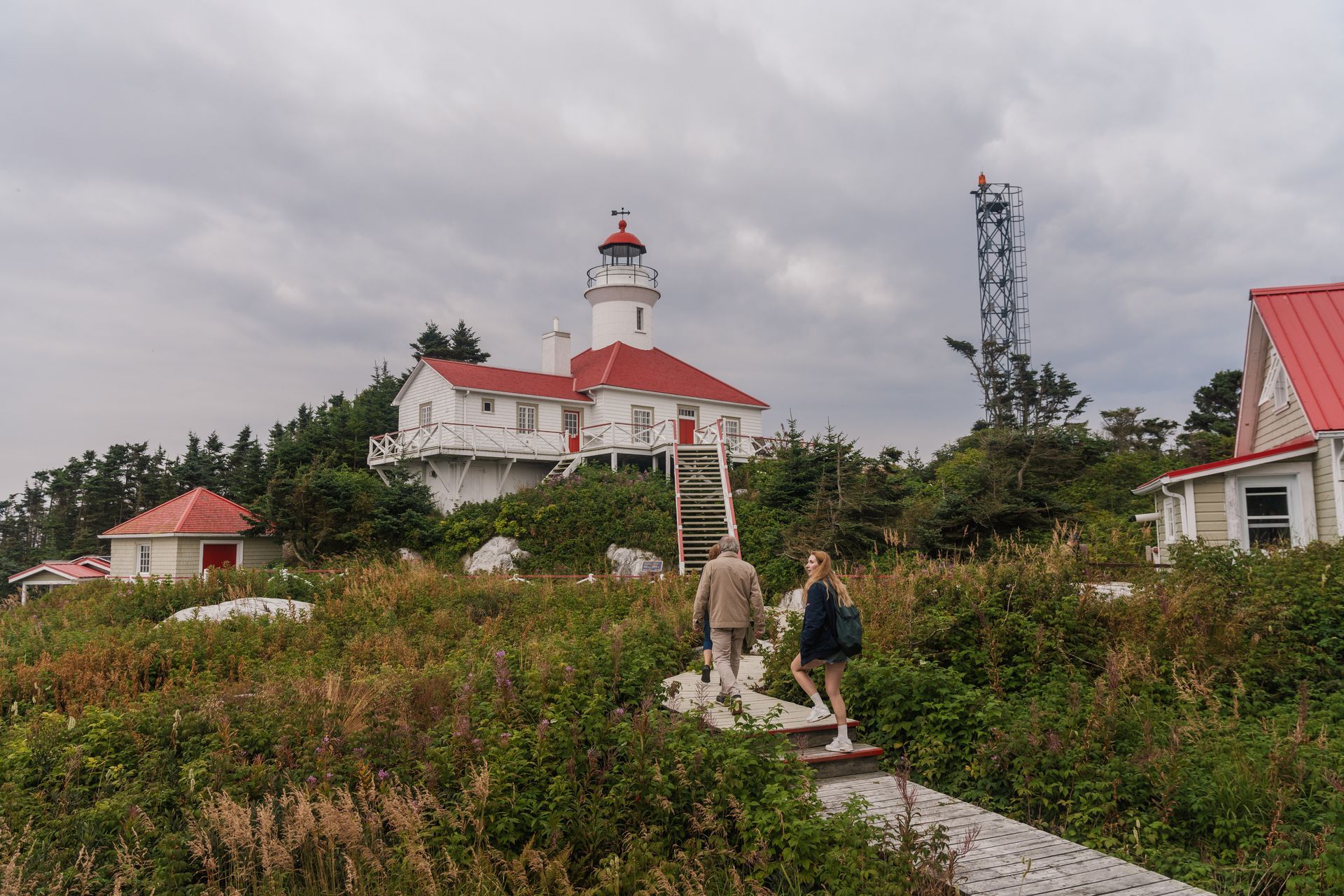 Twee mensen lopen op een bewolkte dag over een pad richting de witte vuurtoren Brandy Pot Island Lighthouse in Quebec, Canada, met een rood dak.