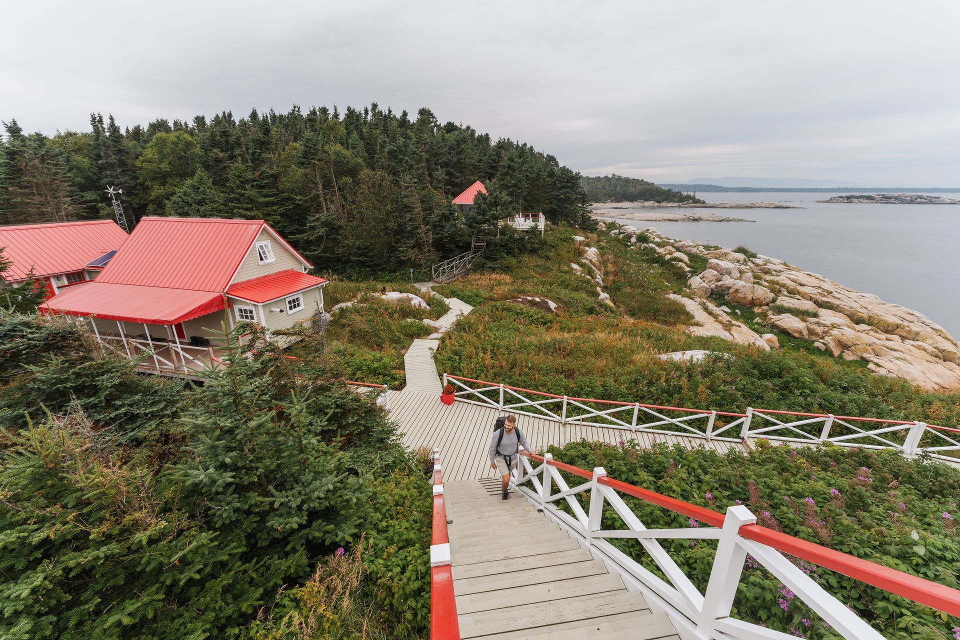 De promenade langs de kust van Brandy Pot Island Lighthouse in Quebec, Canada, met gebouwen met rode daken en bomen, waar mensen over de rotsachtige kustlijn wandelen.