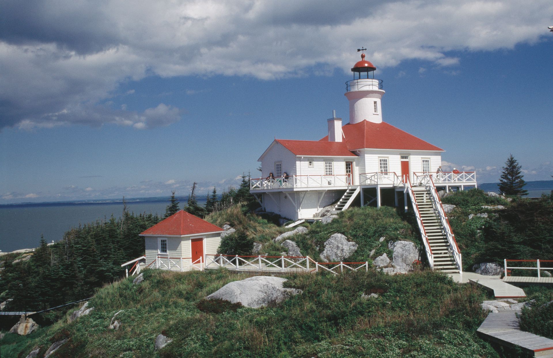 De wit-rode vuurtoren Brandy Pot Island Lighthouse in Quebec, Canada, op een rotsachtige kust onder een bewolkte hemel, met de oceaan op de achtergrond.