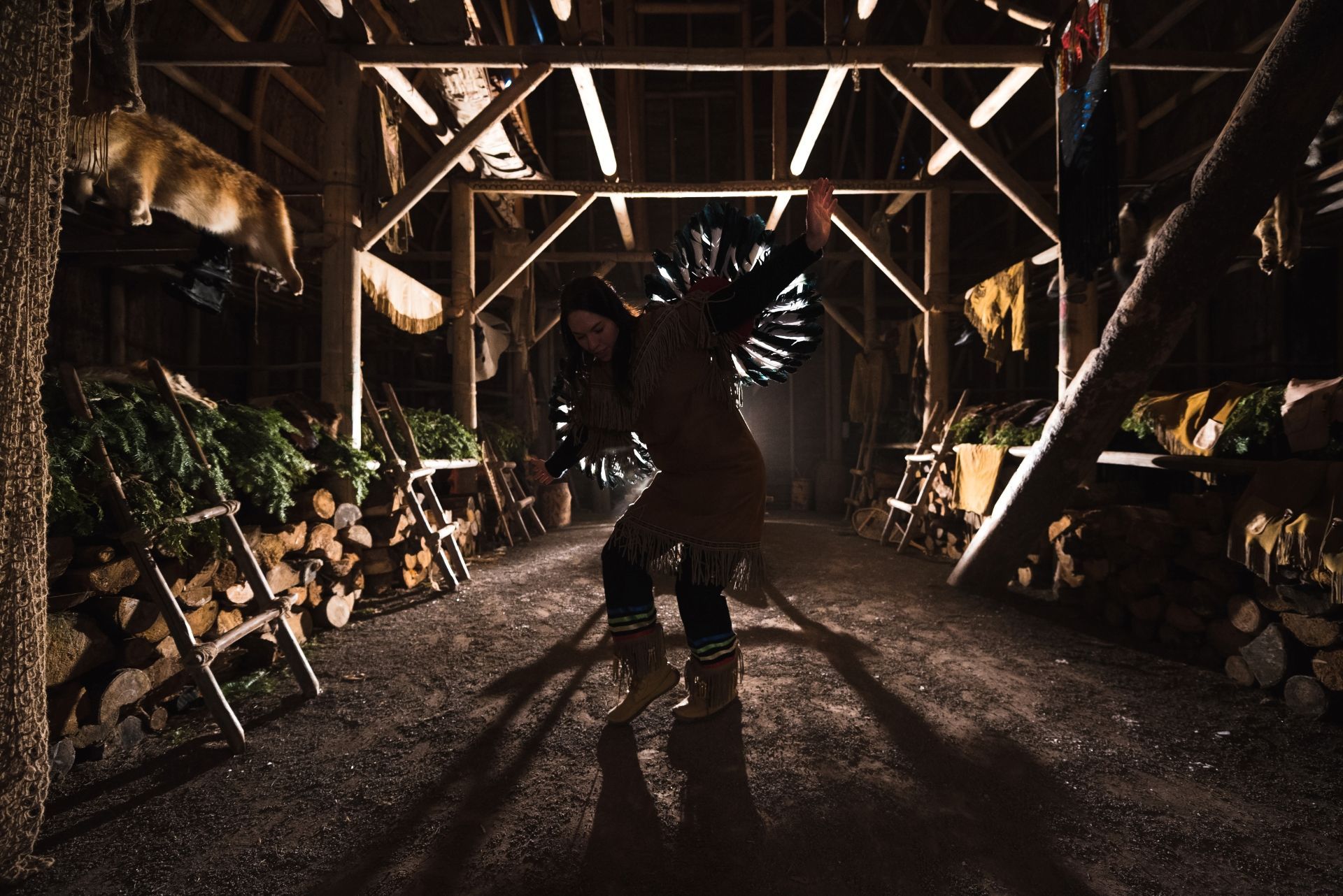 Een danseres in silhouet in Huron Traditional Site ONHOÜA CHETEK8E in Canada, verlicht door warme lampen en omgeven door planten.