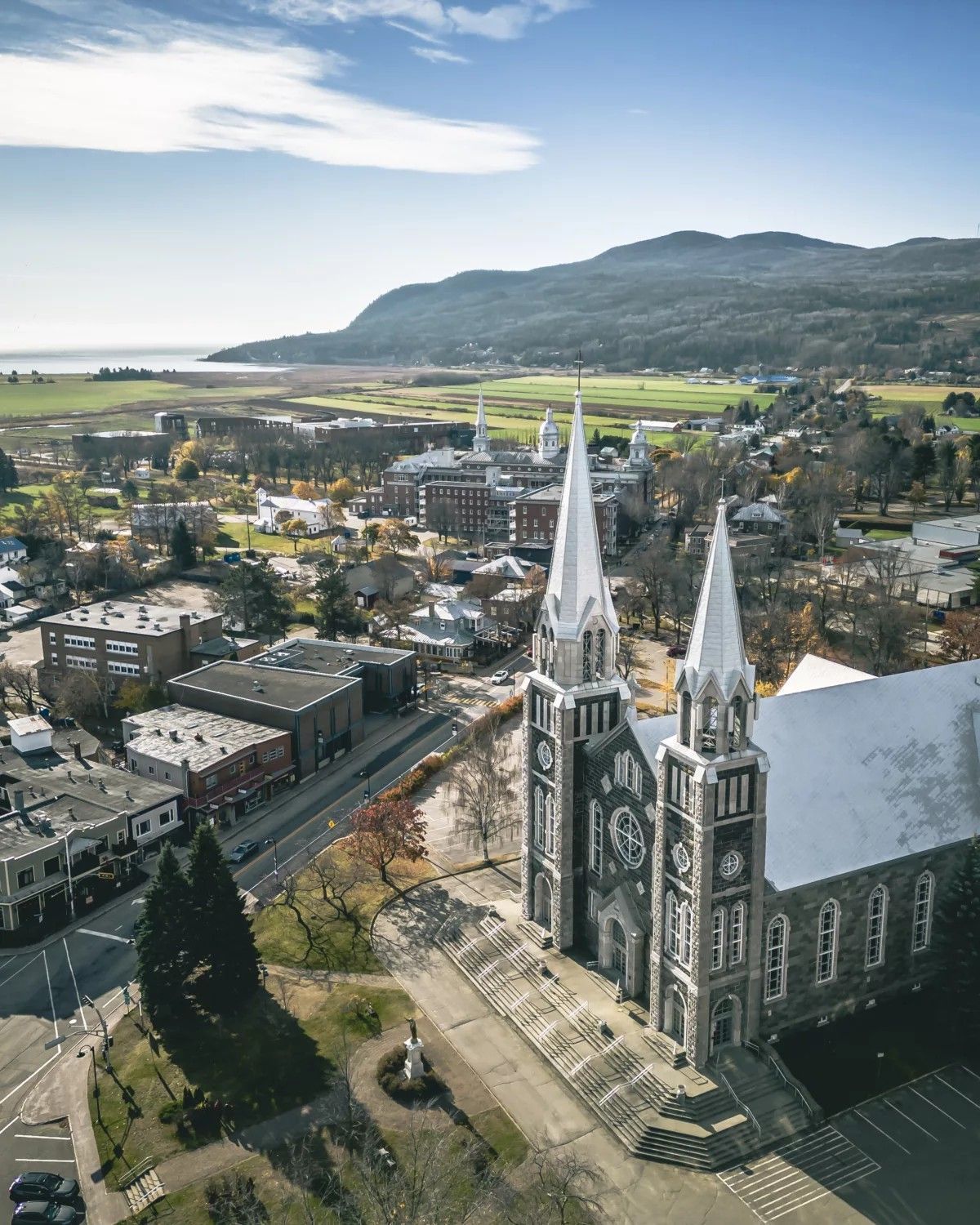 Luchtfoto van de gotische kerk in Baie-Saint-Paul in Charlevoix, Canada, naast een stad met bergen en velden op de achtergrond.