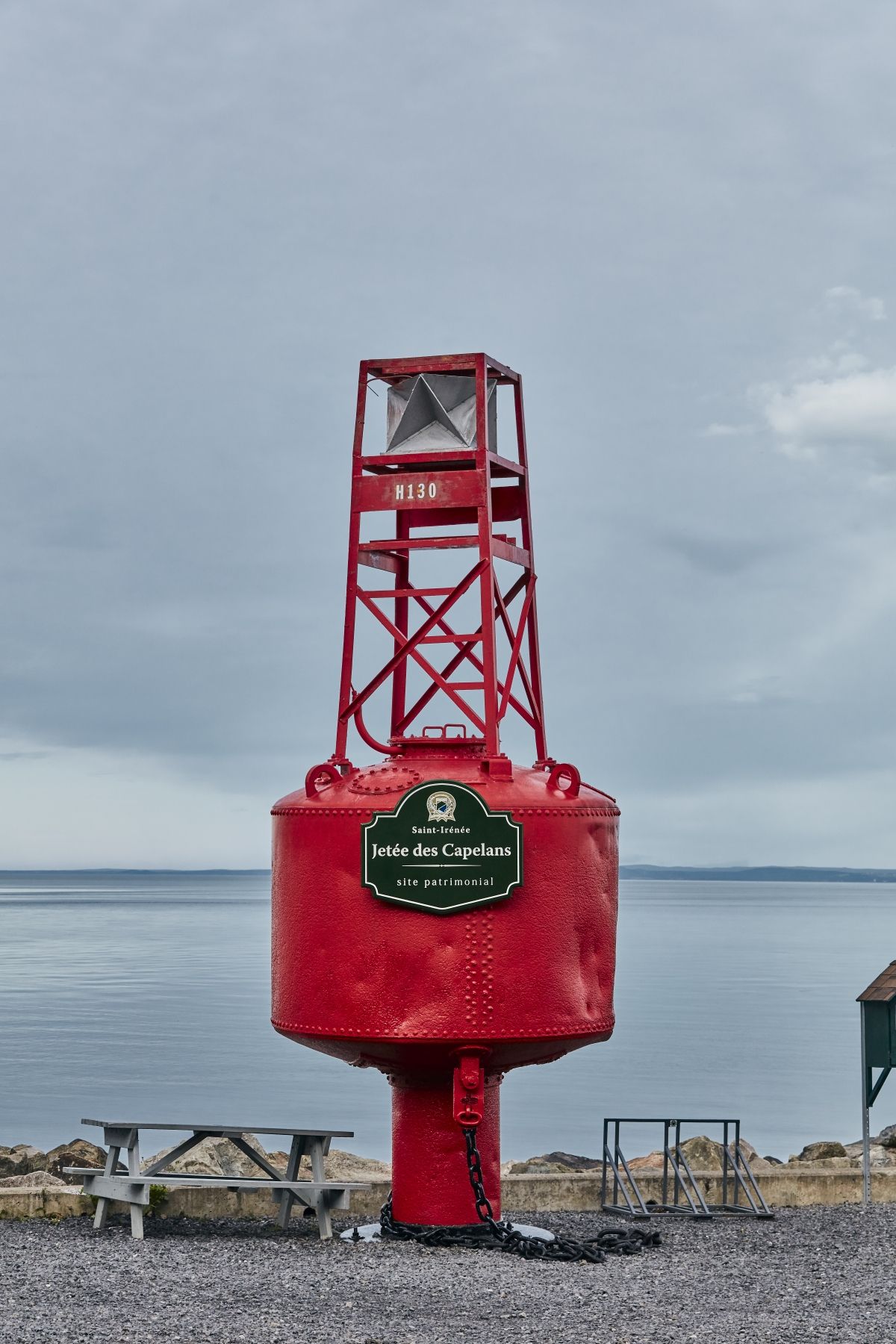 Rode navigatieboei aan de waterkant op een rotsachtige kustlijn van de St. Lawrence River in Quebec, Canada, onder een bewolkte hemel.
