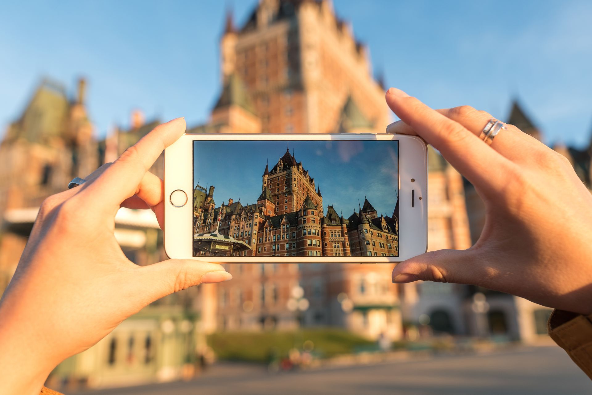 Handen die een smartphone vasthouden om Château Frontenac in Quebec bij zonsondergang te fotograferen.