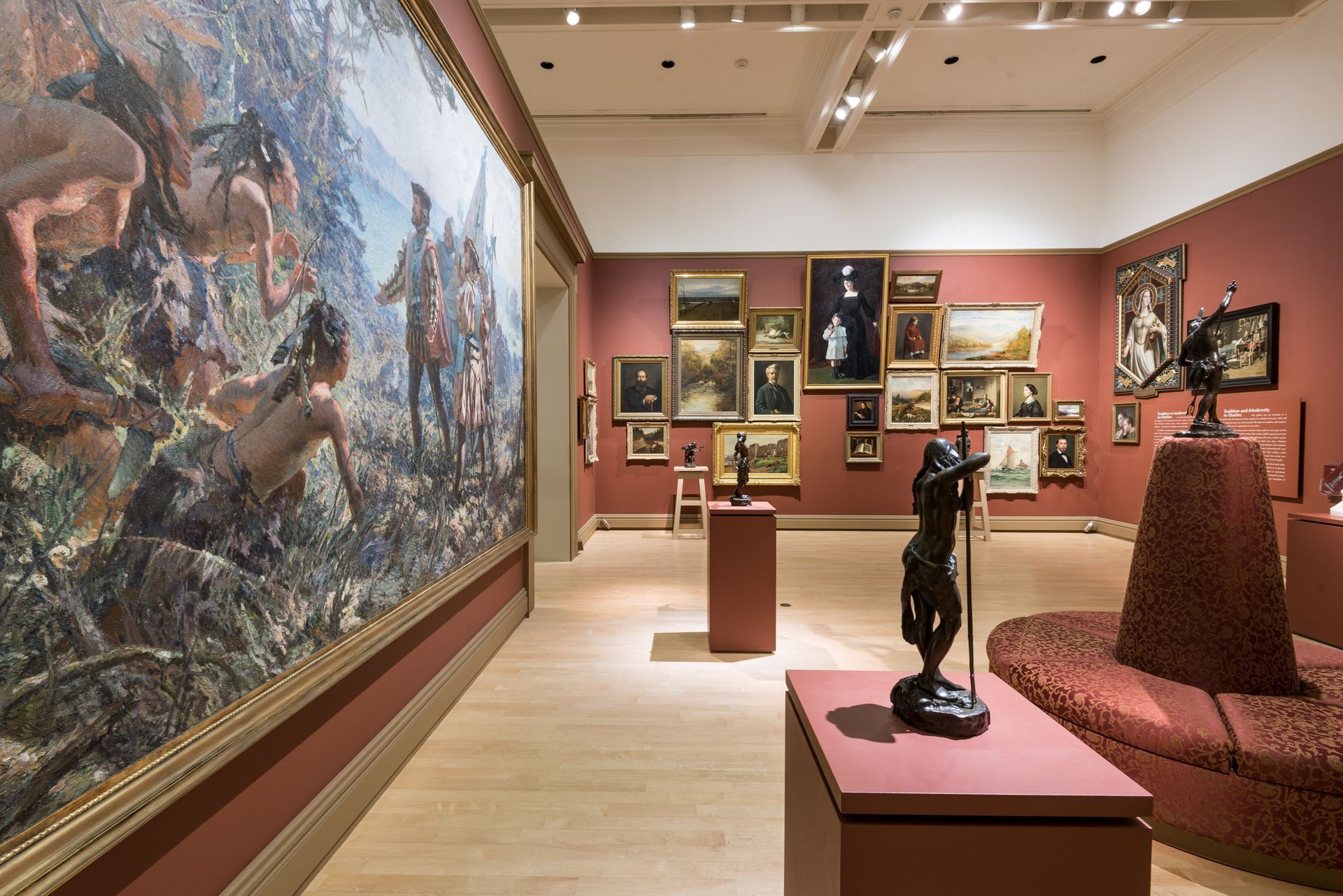 Een kamer in het Musée National des Beaux-Arts du Québec met een grote muurschildering, ingelijste schilderijen en sculpturen op roze sokkels.