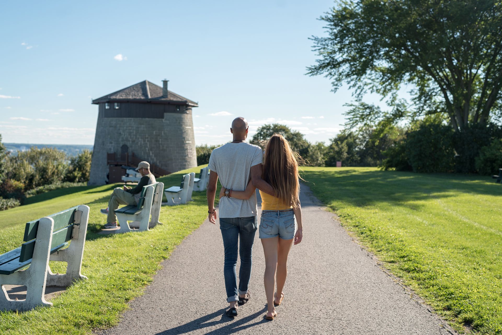 Twee mensen lopen over een grindpad van Plains of Abraham in Quebec richting de stenen toren Martello Tower onder een lauwe hemel.