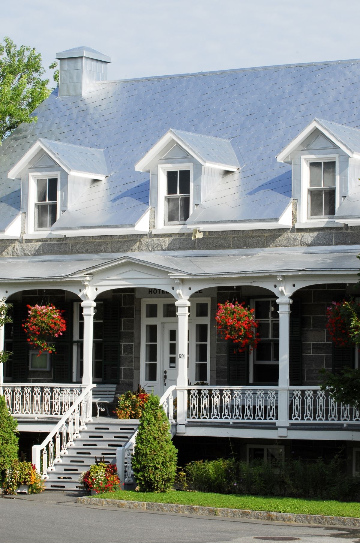 Wit Victoriaans huis Vieux Presbytère de Deschambault in Quebec met blauw dak, veranda en hangende rode bloembakken.