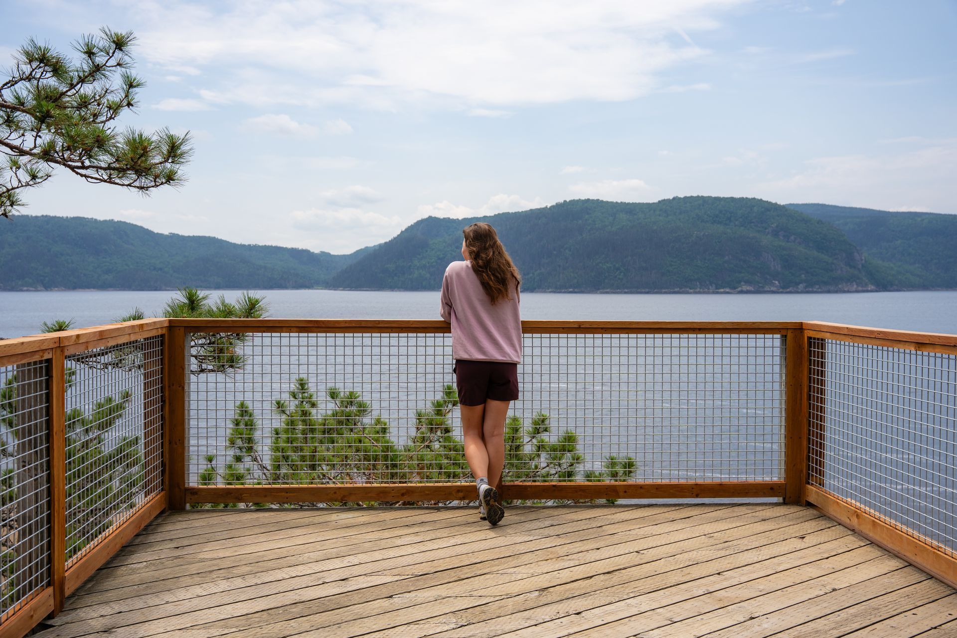 Een persoon staat op een houten vlonder in Canada met uitzicht op een rustig meer en beboste bergen.