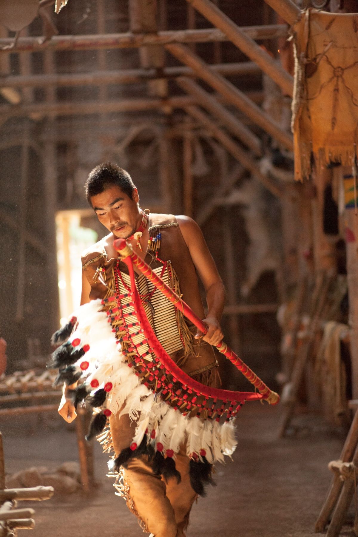 Een artiest in een rood-wit gevederd kostuum danst te midden van de traditionele Longhouse in Huron Traditional Site ONHOÜA CHETEK8E in Canada.