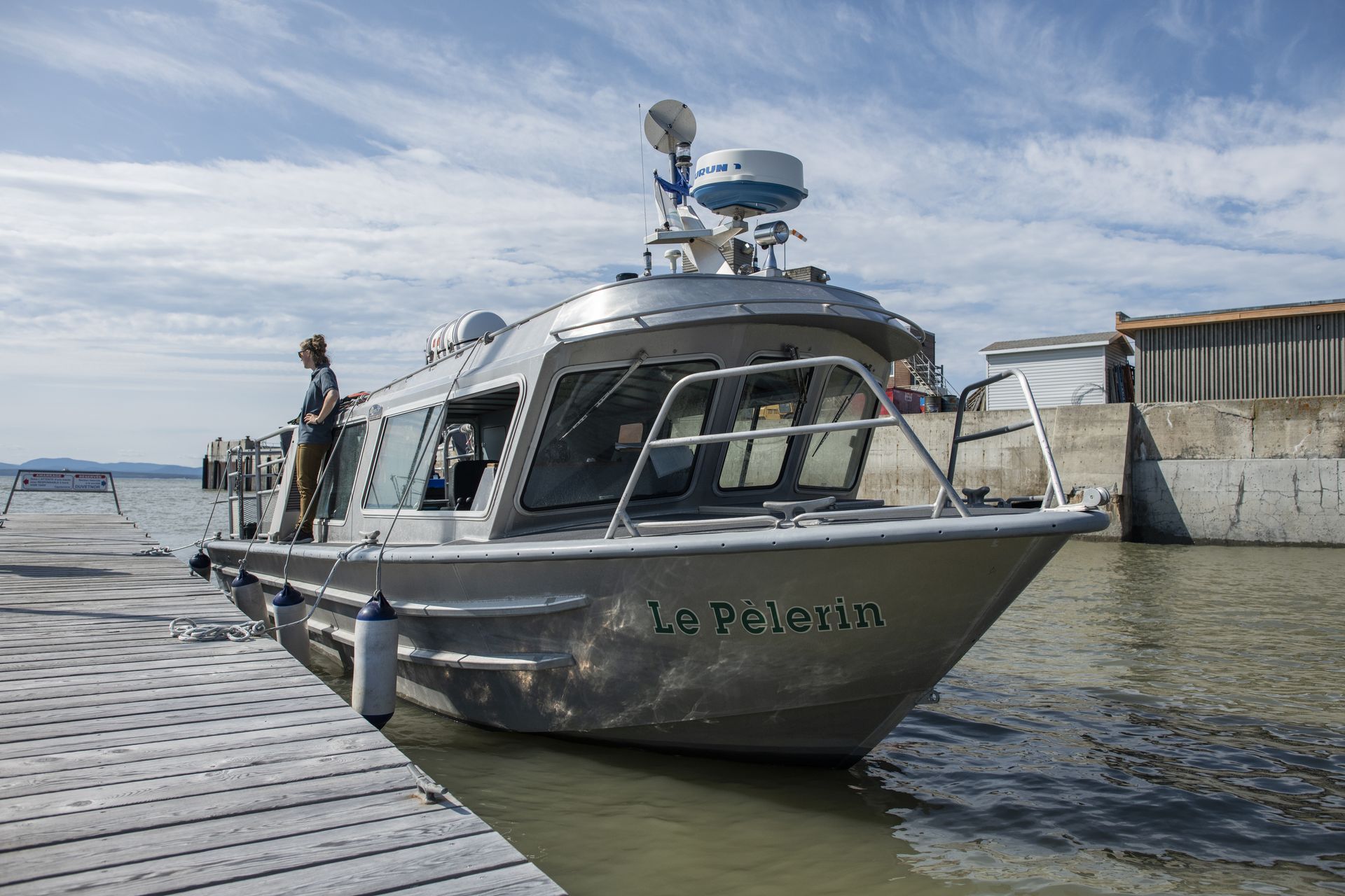 Een zilverkleurige boot ligt aangemeerd in het haventje van Rivière-du-Loup in Quebec, Canada, naast een houten steiger in een rustige haven.