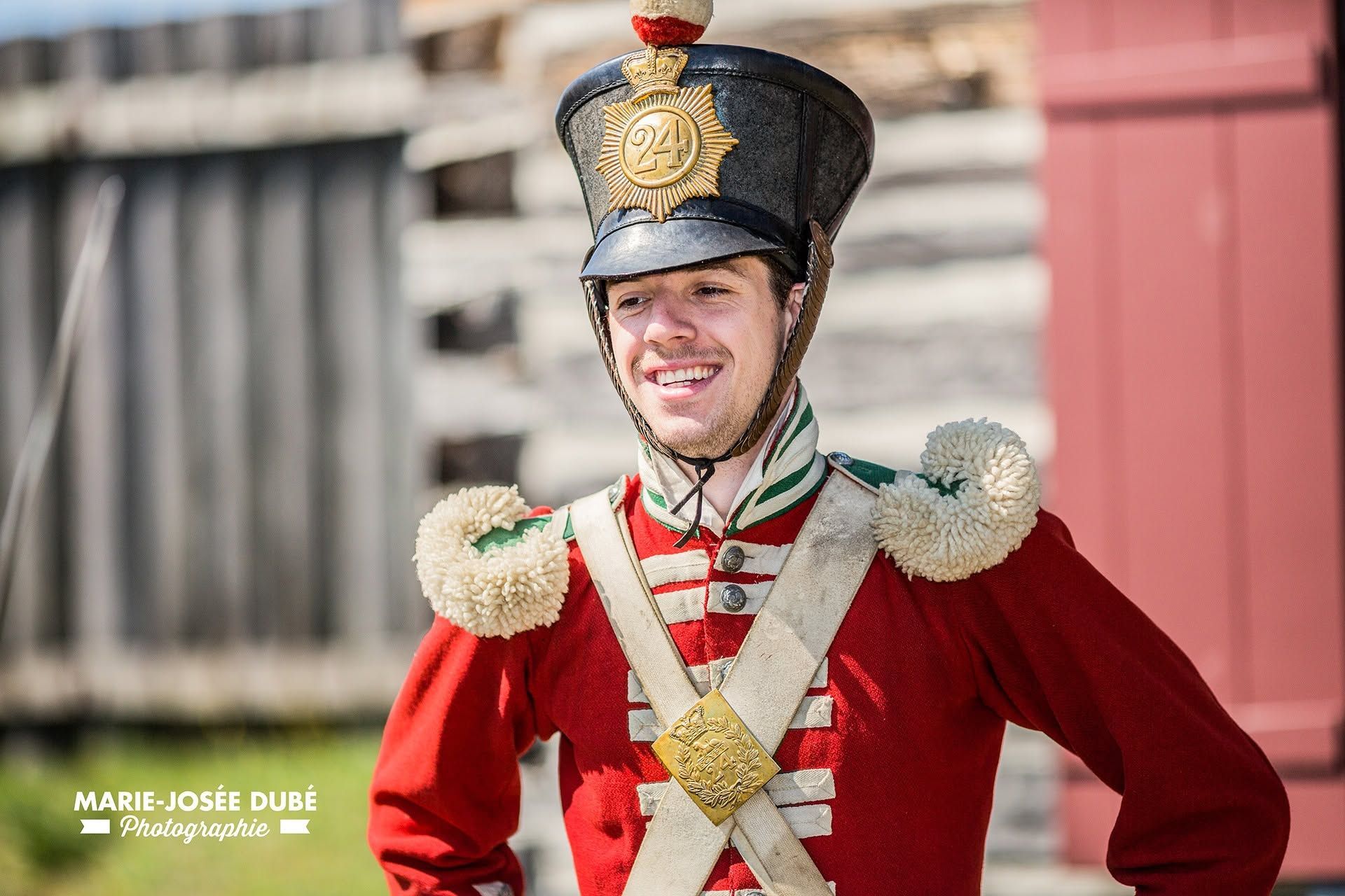 Een man in een rood uniform vanFort Ingall in Quebec, Canada, en een hoge hoed staat buiten te glimlachen.