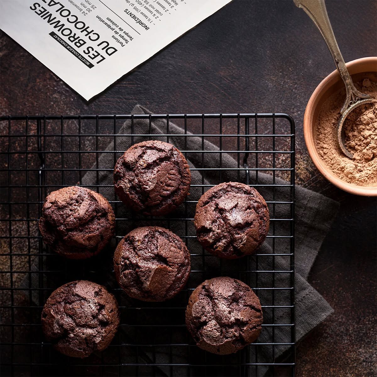 Chocolademuffins op een rooster om af te koelen, naast een kopje cacao en een lepel in Quebec, Canada.