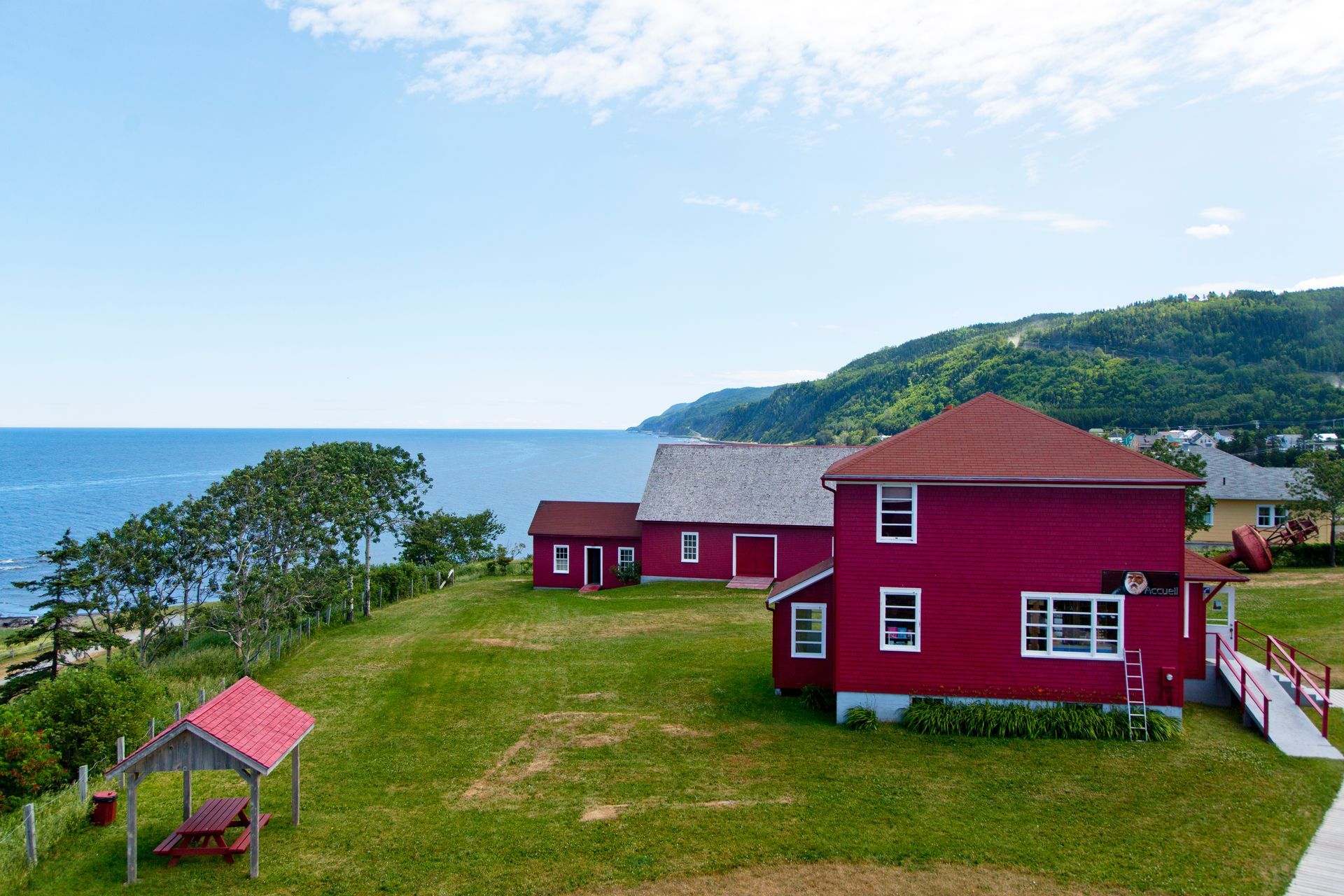 Rode huizen aan zee in Le Martre in Quebec, Canada, op een met gras begroeide klif met uitzicht op de oceaan onder een blauwe hemel.