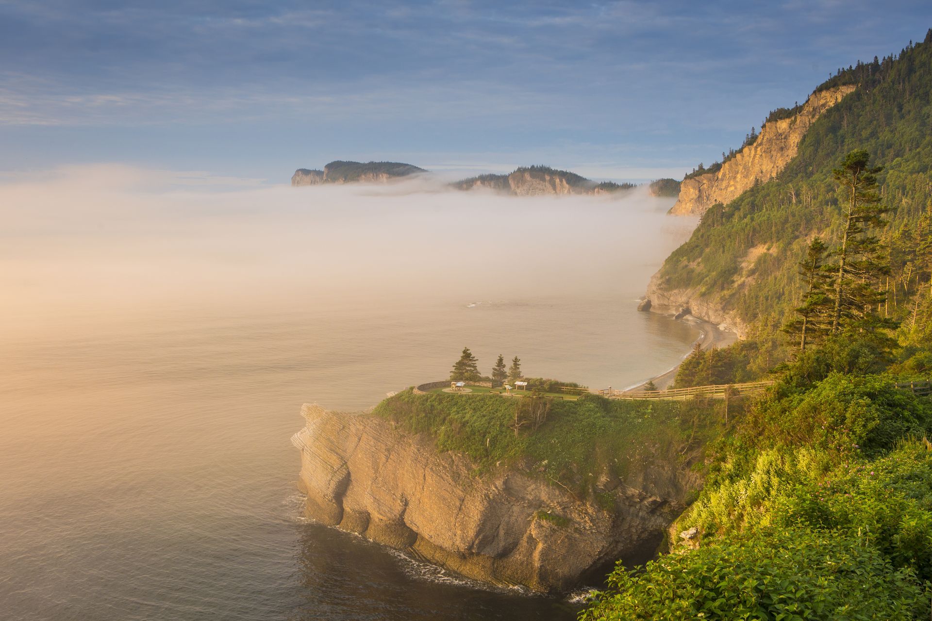 Een klif aan de kust bij Cap Bon-Ami in Quebec, Canada, zonsopgang, met mist boven de zee en een klein grasveldje aan de rand.