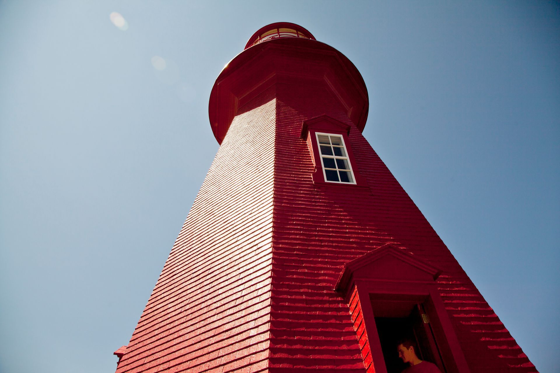 Een laag perspectief van een rode vuurtoren van La Martre in Quebec, Canada tegen een helderblauwe lucht.
