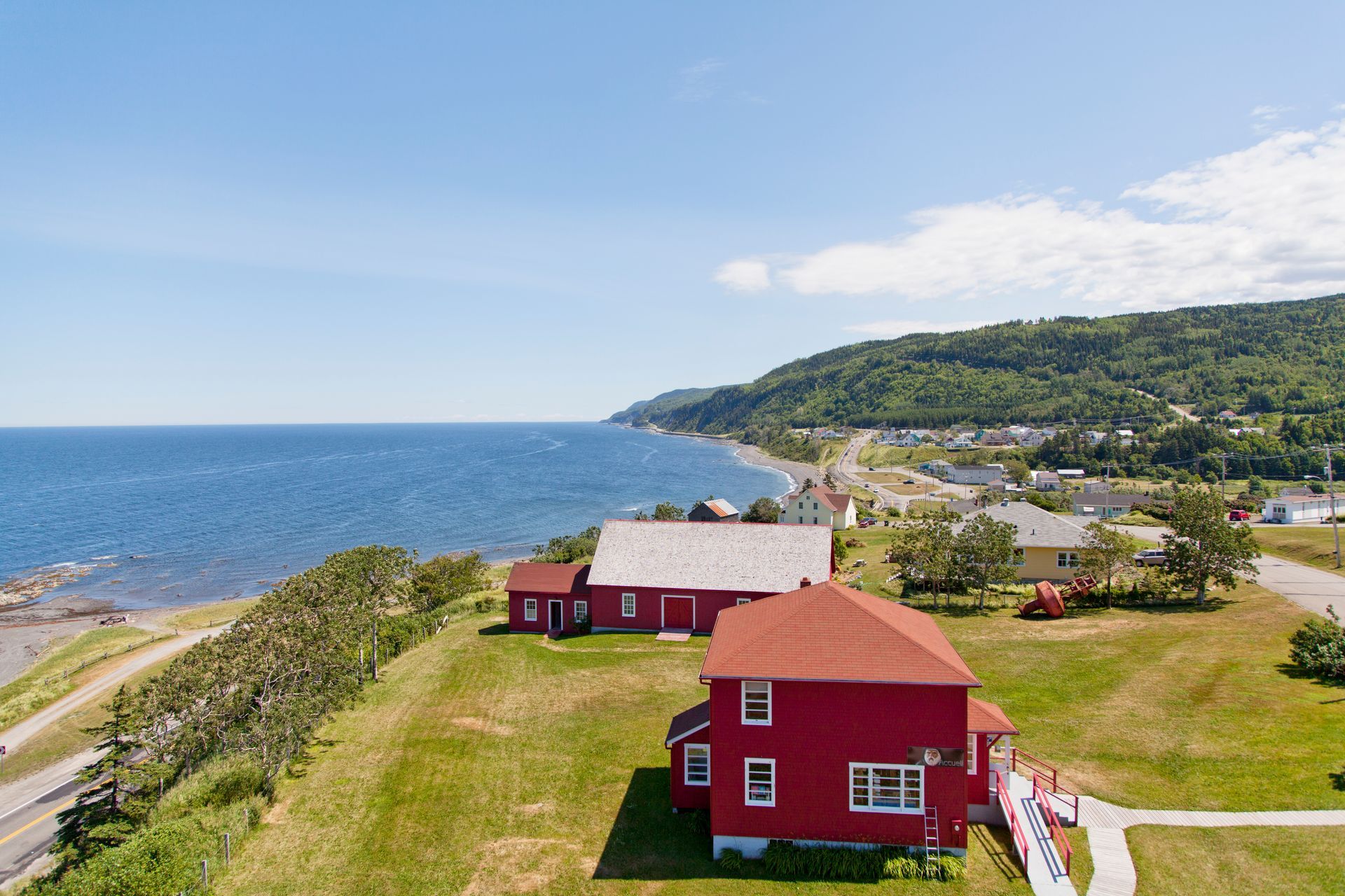 Rood huis in La Martre in Quebec, Canada, op een met gras begroeide klif met uitzicht op de blauwe oceaan en een beboste kustlijn.